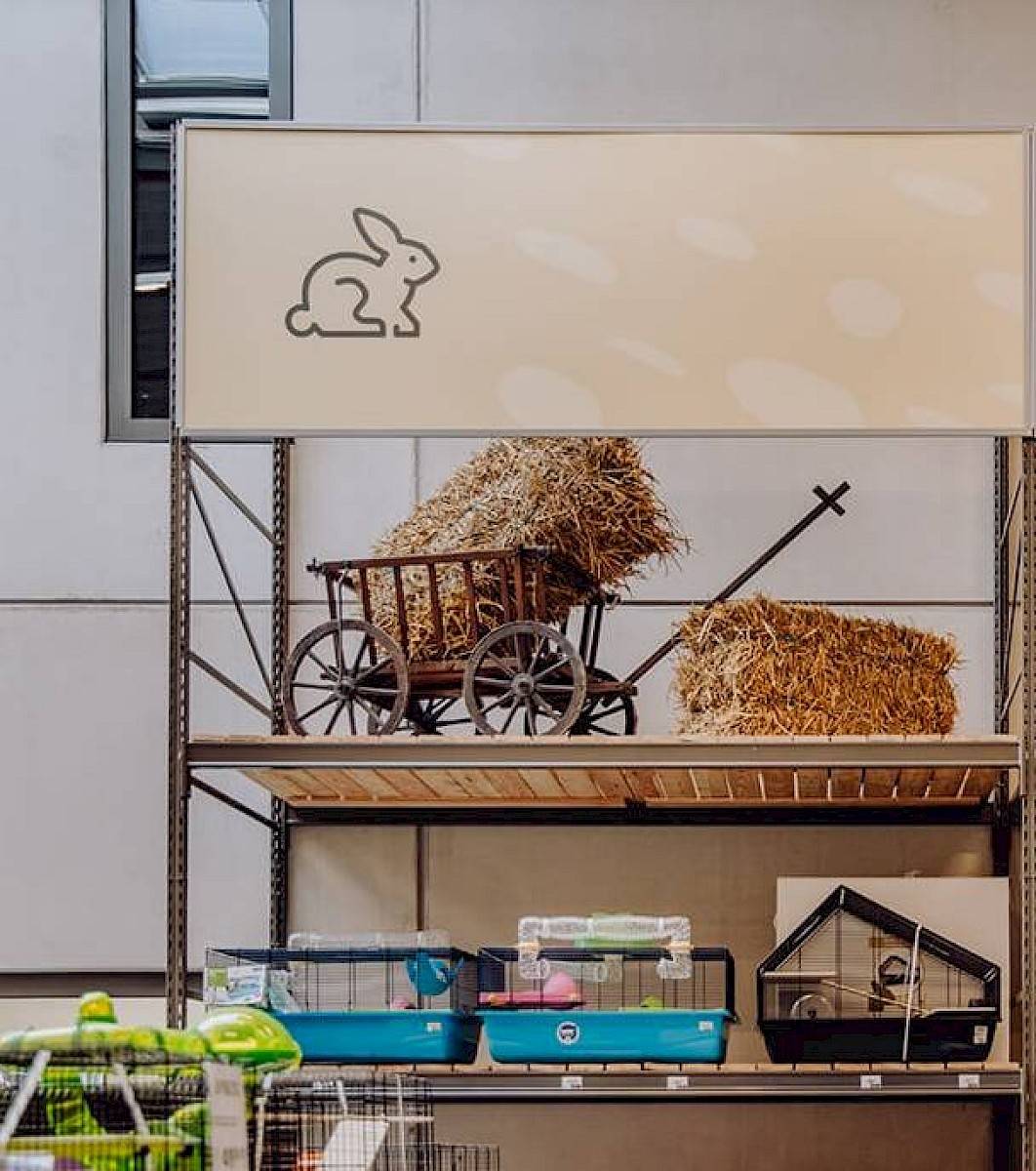 Drie kooien voor knaagdieren uitgestald op een winkelrek, daarboven een kar met hooi in en naast.